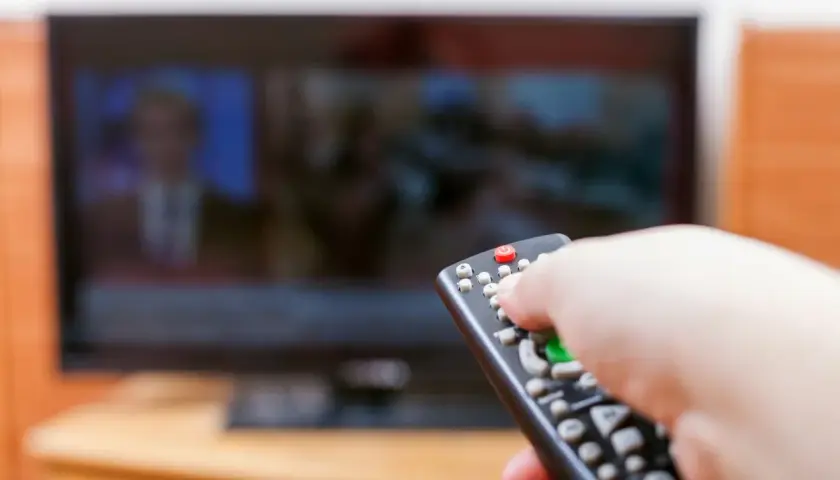 Dłoń z pilotem przed telewizorem, być może to już koniec abonamentu rtv i czas na zmiany.