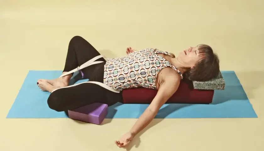 Kvinna i supta baddha konasana med stöd av bolster och block.
