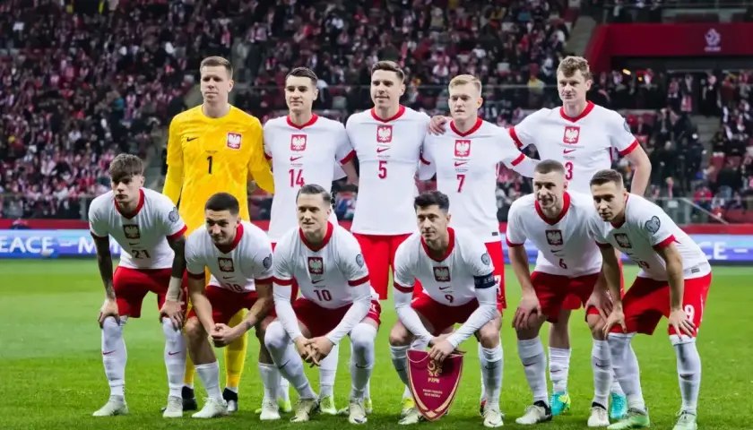 Piłkarze reprezentacji Polski w białych strojach pozują na murawie stadionu.