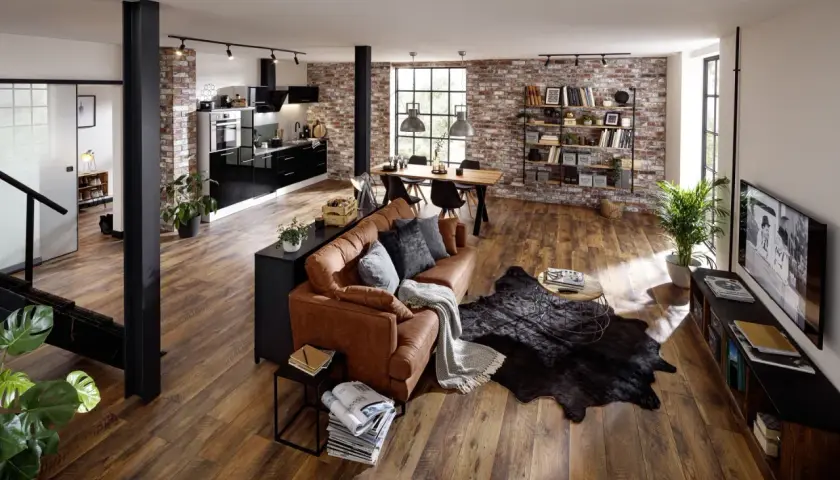 Gemütliches **vintage industrial style wohnzimmer** mit Ledersofa, Holzboden und Ziegelwand. Offene Küche und Essbereich im Hintergrund.