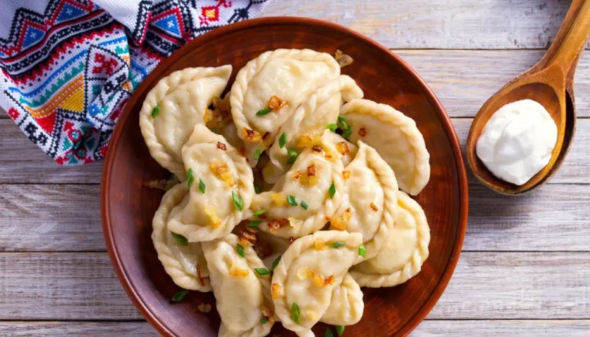 Pyszne pierogi z bryndzą, posypane skwarkami i szczypiorkiem, podane z łyżką śmietany.