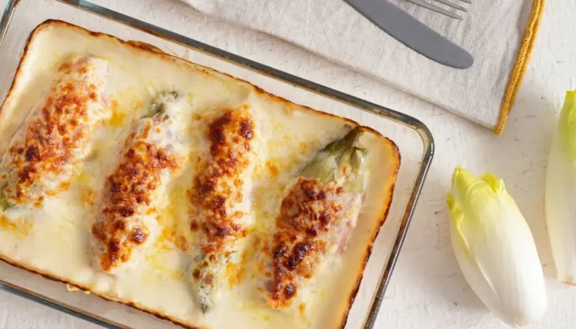 Endivias a la plancha con jamón, gratinadas con queso y bechamel en una fuente de cristal.