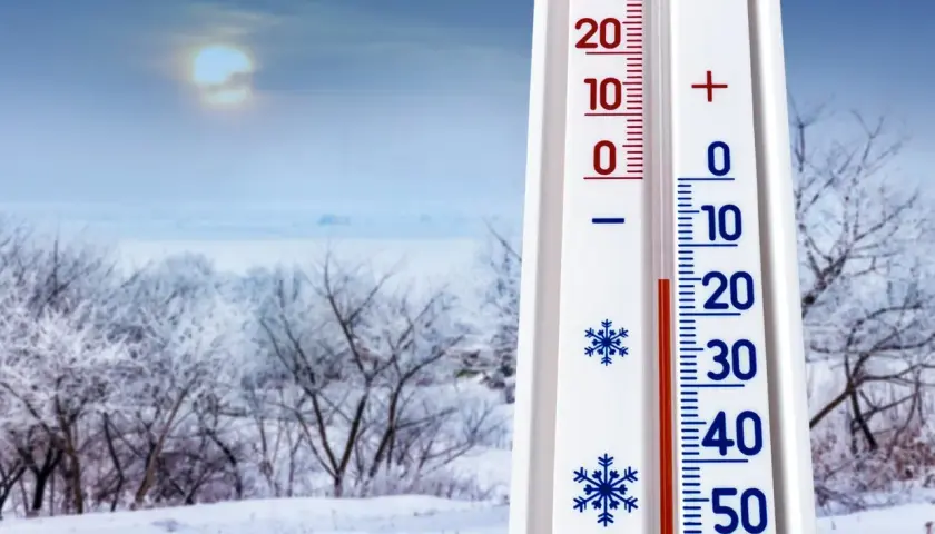 Termometr pokazuje -10°C, co zapowiada mroźną pogodę na styczeń 2026. Zimowy krajobraz z ośnieżonymi drzewami i bladym słońcem.