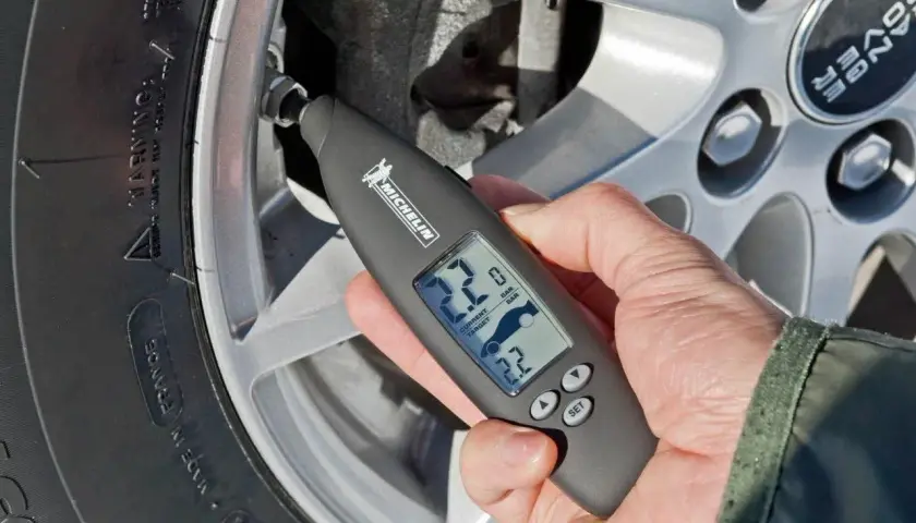 Mano usa un medidor digital Michelin para comprobar la **pegatina presión neumáticos** de un coche.