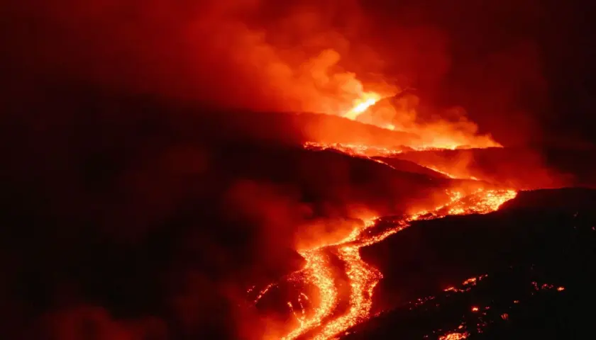 Glühende Lava fließt den Hang eines Vulkans auf Sizilien hinab, umgeben von Rauch und Dunkelheit.