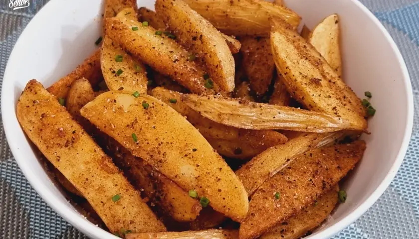 Un tazón lleno de patatas deluxe crujientes, sazonadas con especias y hierbas frescas.