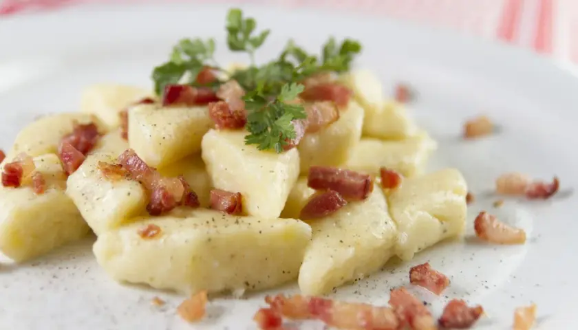 Kopytka z chrupiącym boczkiem i natką pietruszki, posypane pieprzem. Pyszne danie, które aż prosi się, by je zjeść.