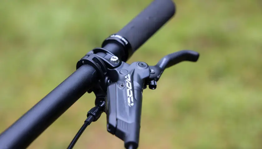 Close-up of a bicycle handlebar with a black brake lever. The lever has "KOO" branding, suggesting a brake fluid comparison.
