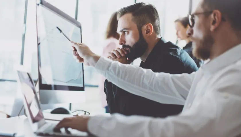 Analityk biznesowy wskazuje na wykres na monitorze, omawiając dane z kolegą.