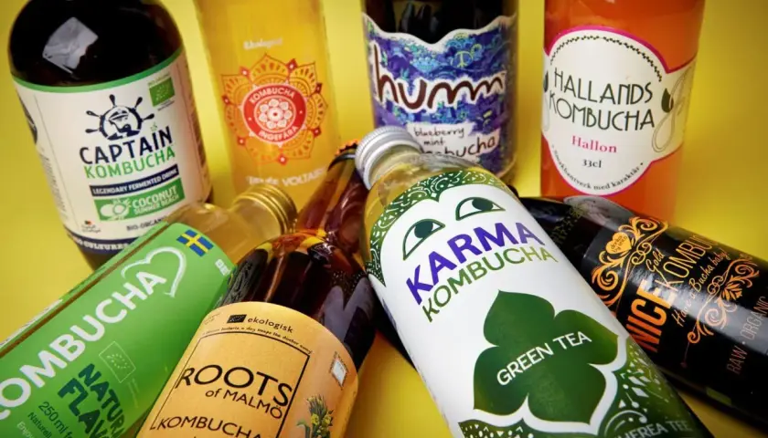 Flera flaskor kombucha, en dryck som många anser vara nyttig, ligger utspridda. Olika märken som Captain Kombucha, Karma Kombucha och Hallands Kombucha syns.