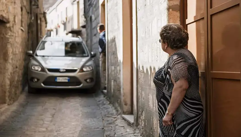 Navigating narrow Italian streets: a silver car is parked in a tight alleyway. Tips for driving in Italy for the first time include being prepared for tight squeezes.