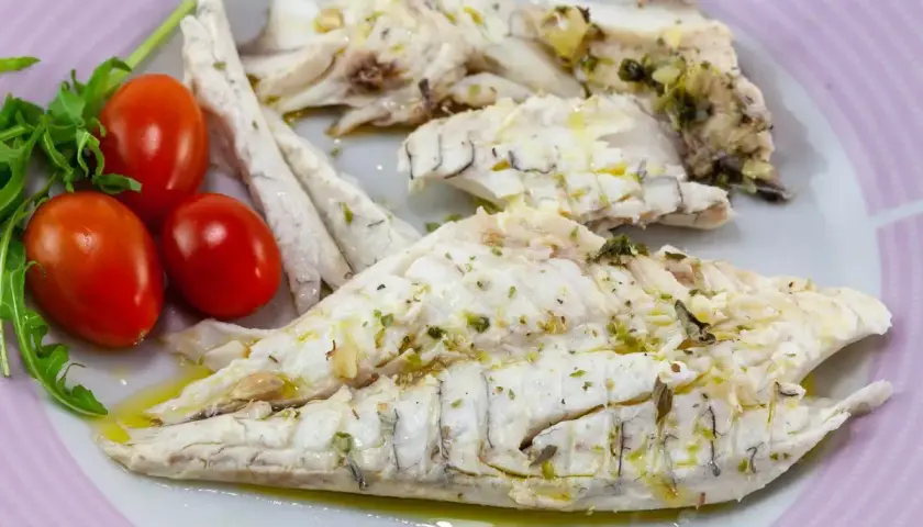 Delizioso branzino in padella, cotto alla perfezione e condito con erbe aromatiche. Servito con pomodorini freschi e rucola.