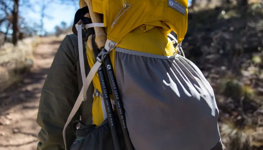 Kijki trekkingowe przymocowane do żółtego plecaka Gossamer Gear. Paski i siatkowa kieszeń pomagają w transporcie.