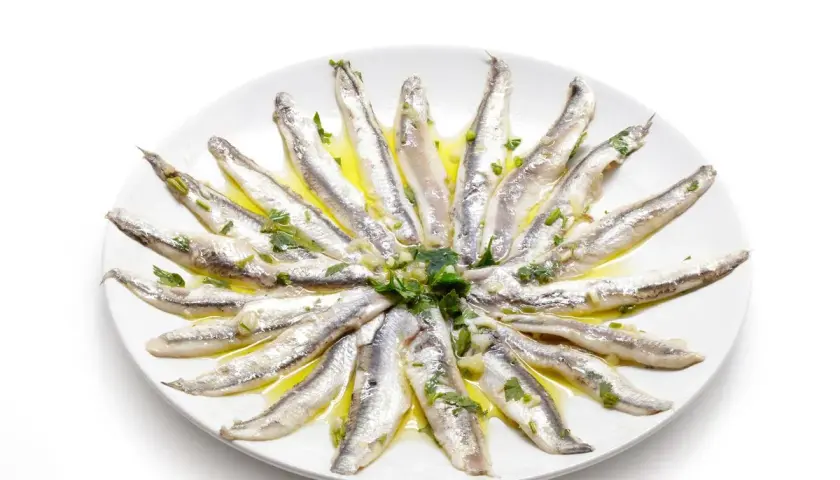 Acciughe al verde disposte a raggiera su un piatto bianco, condite con olio, aglio e prezzemolo.