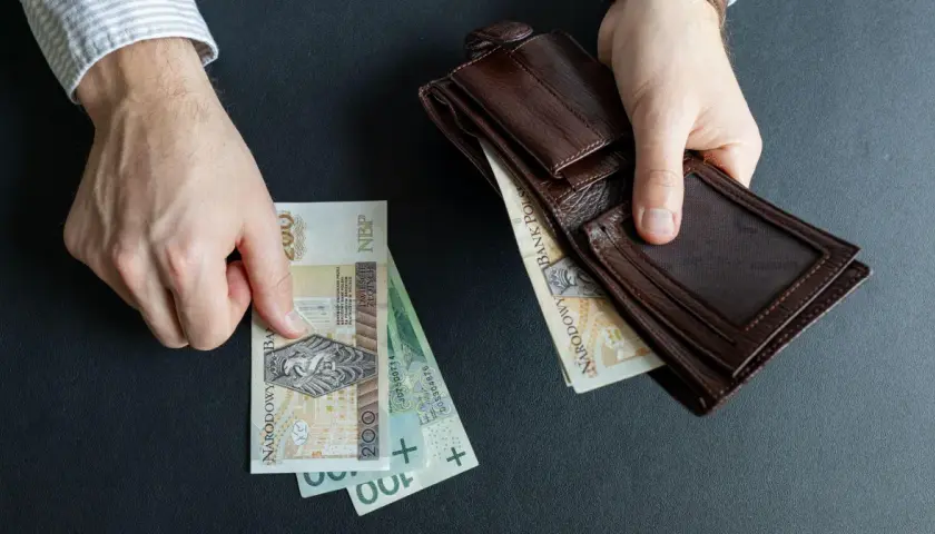 Ręce trzymają polskie banknoty i brązowy portfel. Czy to początek wzrostu renty alkoholowej o 5% od marca 2026?