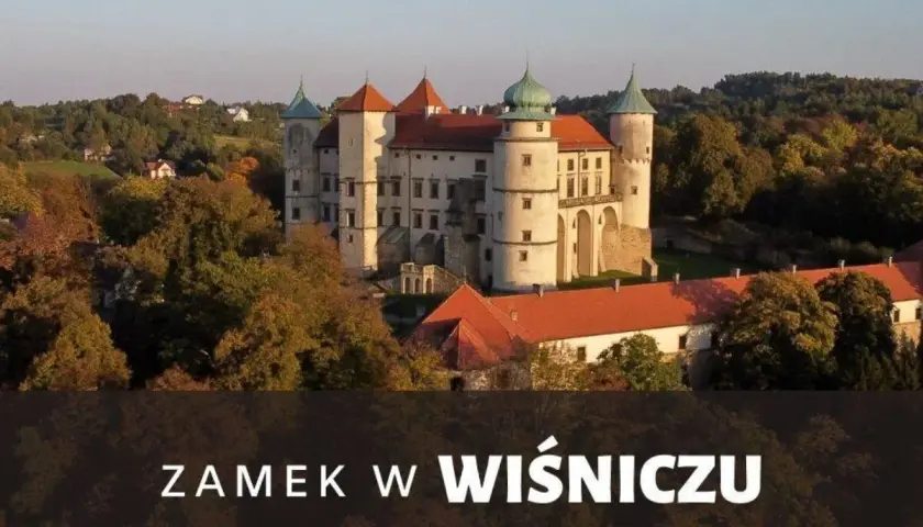 Majestatyczny zamek Wiśnicz otoczony jesiennymi drzewami, z charakterystycznymi wieżami i czerwonymi dachami.