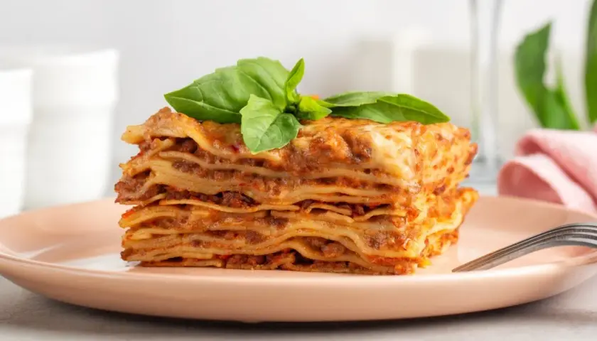 Pyszna, wielowarstwowa lasagne z mięsnym sosem i serem, udekorowana bazylią. Idealny przepis na obiad.
