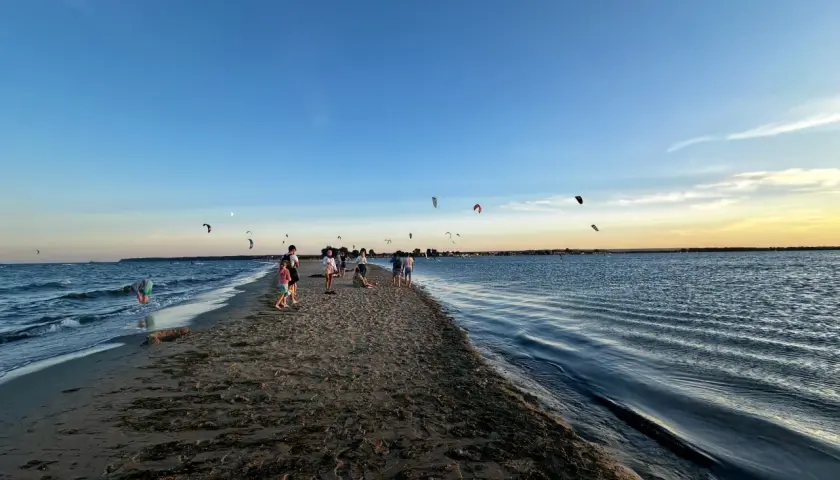 Ludzie spacerują po piaszczystym cyplu Rewskim, gdzie można podziwiać kitesurferów. Jak dojechać? To proste, wystarczy kierować się nad morze.
