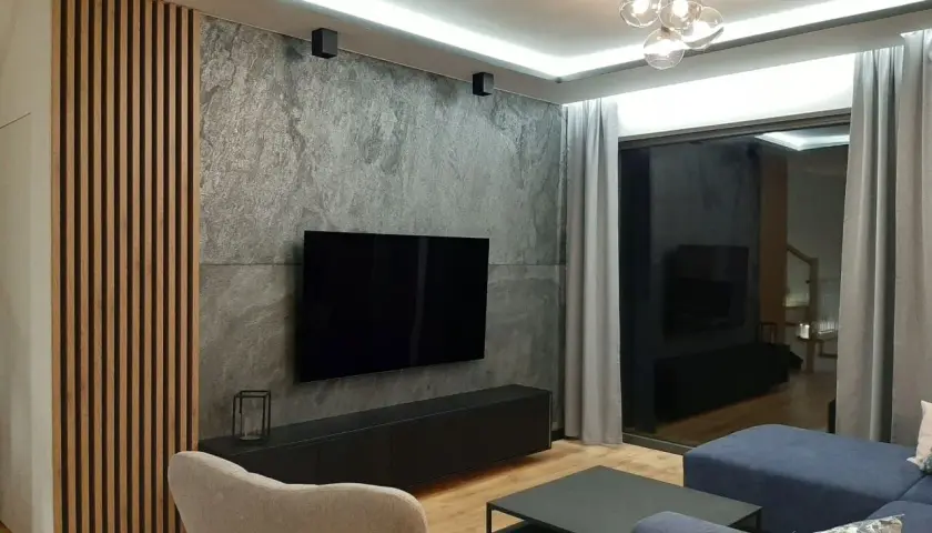Nowoczesny salon z betonem architektonicznym, który świetnie komponuje się z drewnianymi lamelami i granatową sofą.