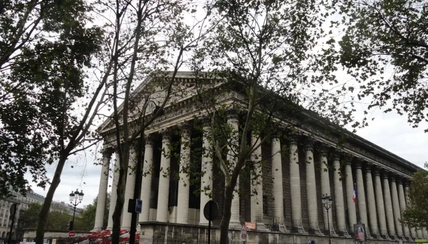 Kościół Madeleine w Paryżu z kolumnadą i drzewami na pierwszym planie.