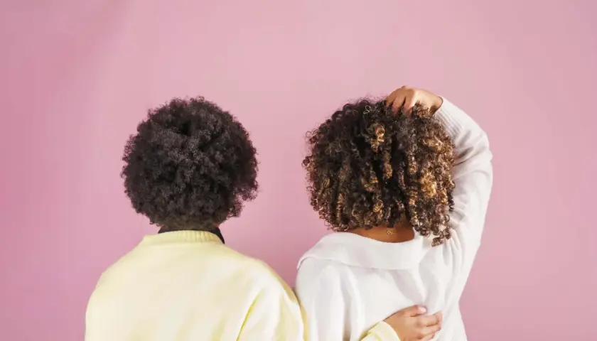Dos personas con cabello rizado, una con afro oscuro y otra con rizos castaños, muestran la belleza natural de su cabello, quizás inspiradas por el método no poo.
