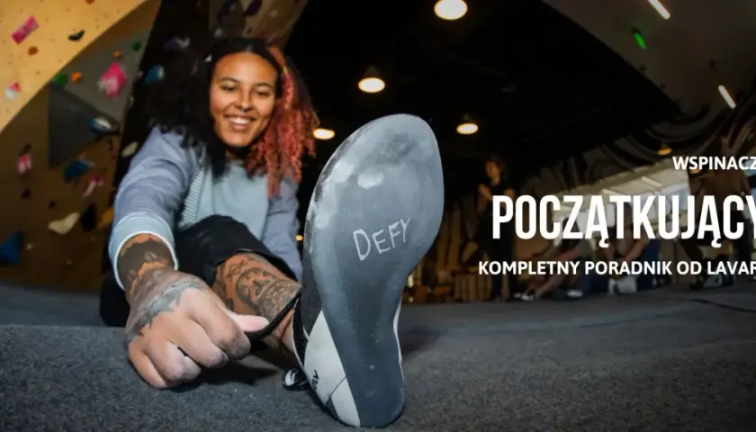 Uśmiechnięta kobieta zakłada buty do wspinaczki na ściance. Dowiedz się, bouldering co to jest i jak zacząć.