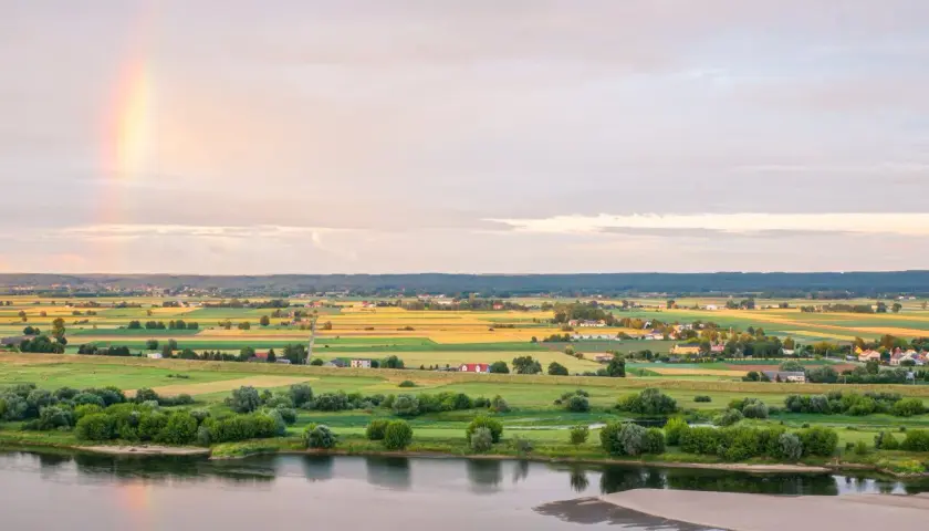 Krajobraz Kociewia nad rzeką, pola uprawne, domy i tęcza na niebie.