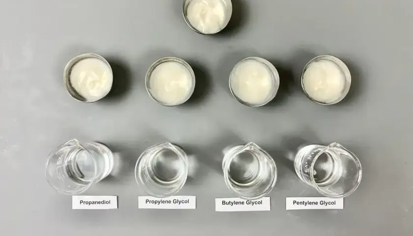 Sześć próbek kremów w małych pojemnikach i cztery zlewki z płynami: propanediol, glikol propylenowy, **butylene glycol** i pentylene glycol.