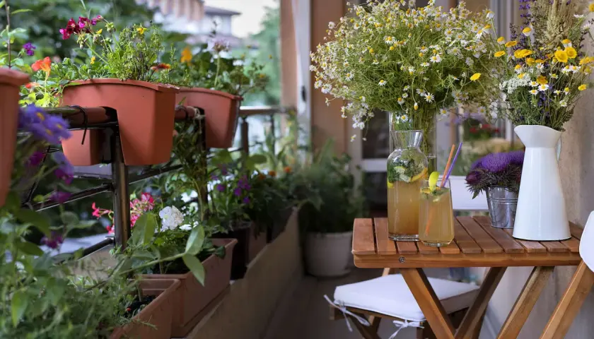 Blumenkästen mit bunten Blüten und Kräutern bieten tolle balkonbepflanzung ideen. Ein Tisch mit erfrischendem Getränk und Blumensträußen lädt zum Verweilen ein.