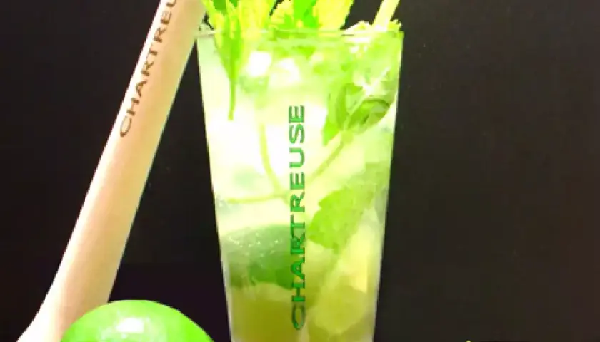 Un verre de cocktail Chartreuse, garni de menthe fraîche et de citron vert, prêt à être dégusté.