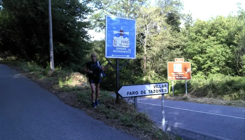 Mujer junto a señal de "El Faro de Tazones" y otra de "Villar, Faro de Tazones".