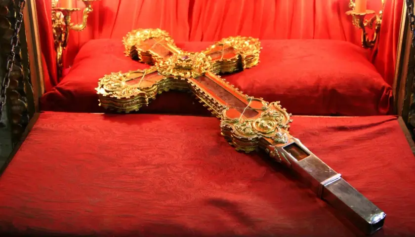 Cruz de Caravaca dorada y enjoyada, expuesta sobre terciopelo rojo en el monasterio de Santo Toribio de Liébana.