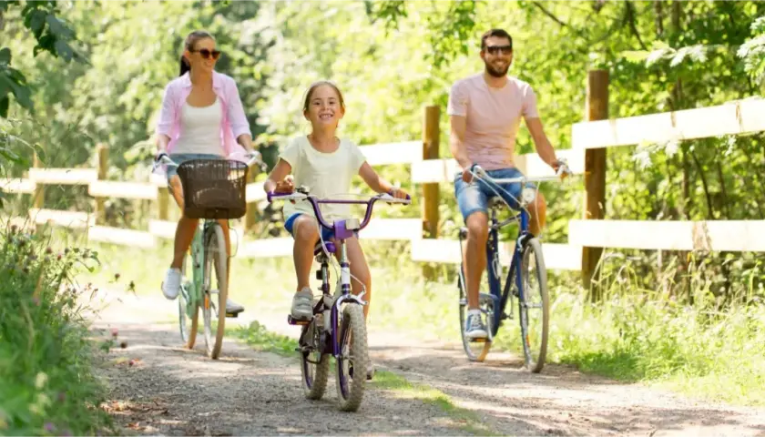 Rodzina cieszy się rodzinną wycieczką rowerową po malowniczych Mazurach. Uśmiechnięta dziewczynka na rowerze, mama i tata jadą leśną ścieżką.