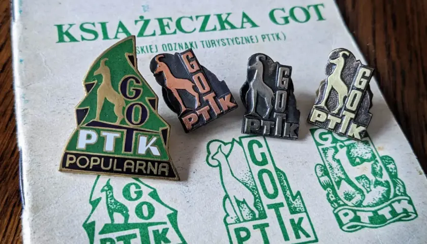 Książeczka GOT z odznakami turystycznymi PTTK. Widoczne cztery odznaki z kozicą i napisem GOT PTTK w różnych kolorach.