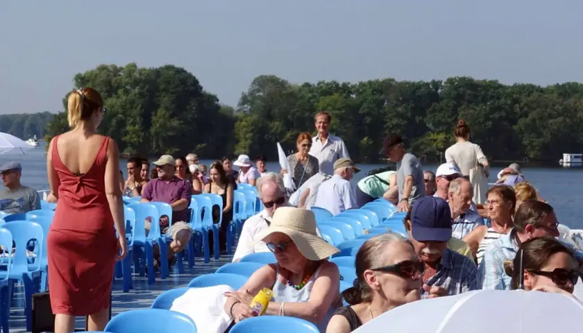 Menschen auf einem Schiff genießen eine Muttertag Unternehmung. Sie sitzen auf blauen Stühlen und blicken auf das Wasser.