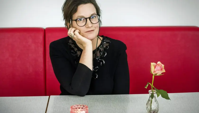 Agnes Lidbeck med familj, en kvinna med glasögon och en blomma på bordet, sitter vid ett rött bås.