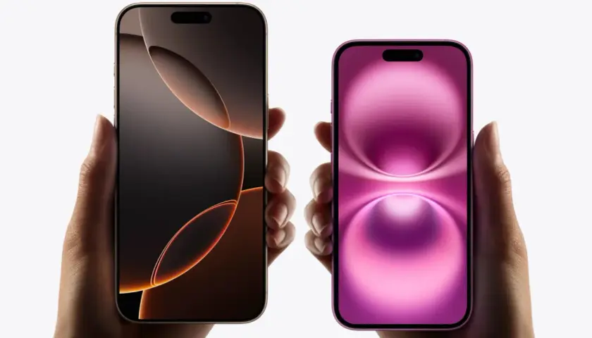 Dwie dłonie trzymają dwa iPhone'y. Jeden ma ciemny ekran z pomarańczowymi akcentami, drugi różowy. Oba modele mają dynamiczną wyspę.