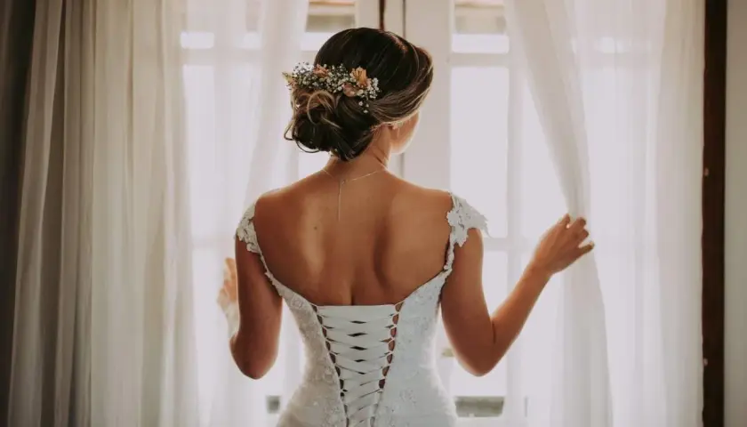 Novia con un juvenil recogido de boda adornado con flores, luciendo su espalda con un corsé de encaje.