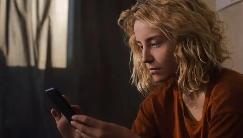Zamyślona dziewczyna z blond włosami trzyma telefon, czekając na wiadomość. Może ta dziewczyna nie odpisuje.