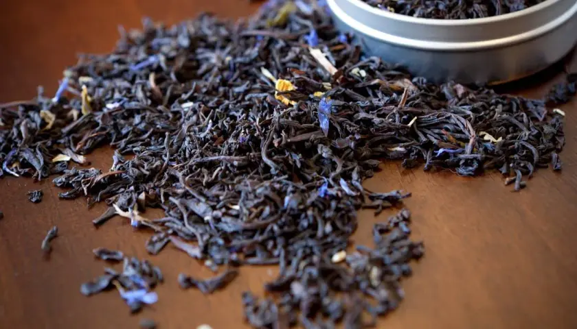Garść liści aromatycznej herbaty earl grey, z niebieskimi płatkami chabru, rozsypana na drewnianym blacie.