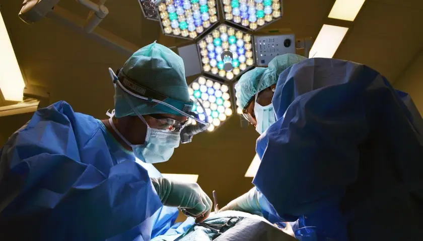 Chirurdzy w sterylnych strojach pracują pod jasnym światłem lampy operacyjnej. Po zabiegu mogą wystąpić narkoza skutki uboczne.