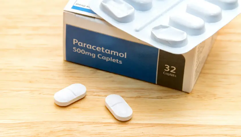 Opakowanie Paracetamolu 500mg, leki na ból kręgosłupa szyjnego, leżą na drewnianym blacie obok dwóch tabletek.