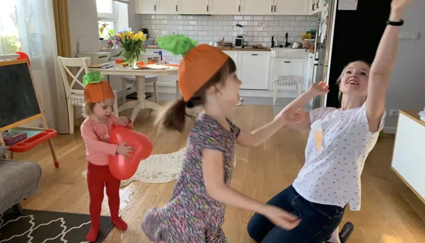 Dzieci w czapkach marchewek bawią się balonami w kuchni.