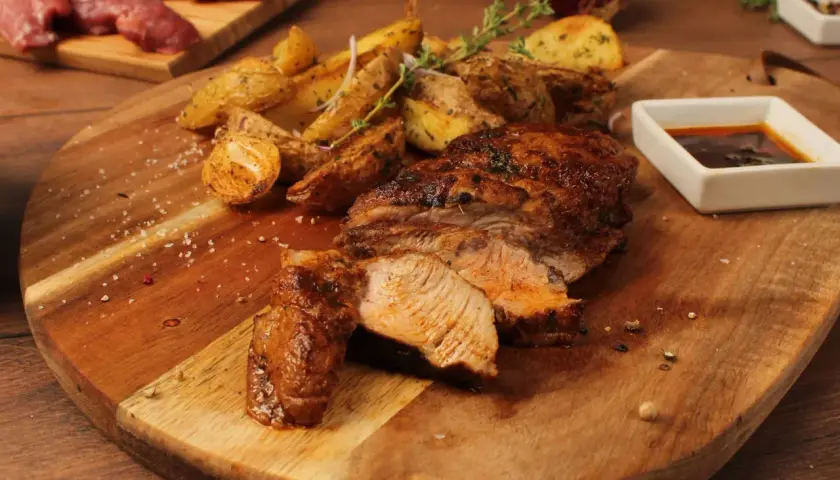 Pluma de porc recette : viande grillée juteuse, pommes de terre rôties et sauce savoureuse sur une planche en bois.