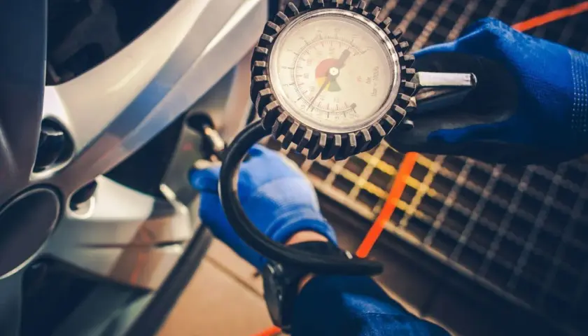 Sprawdzanie ciśnienia w oponach 205/60 r16 za pomocą manometru. Dłoń w niebieskiej rękawiczce podłącza wężyk do wentyla.