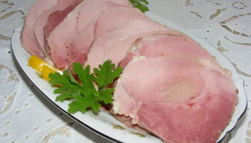 Plasterek gotowanej szynki z plasterkiem cytryny i natką pietruszki na talerzu.