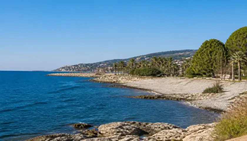 Côte rocheuse et mer bleue près d'une ville côtière en Italie, Imperia, avec des palmiers et des pins.