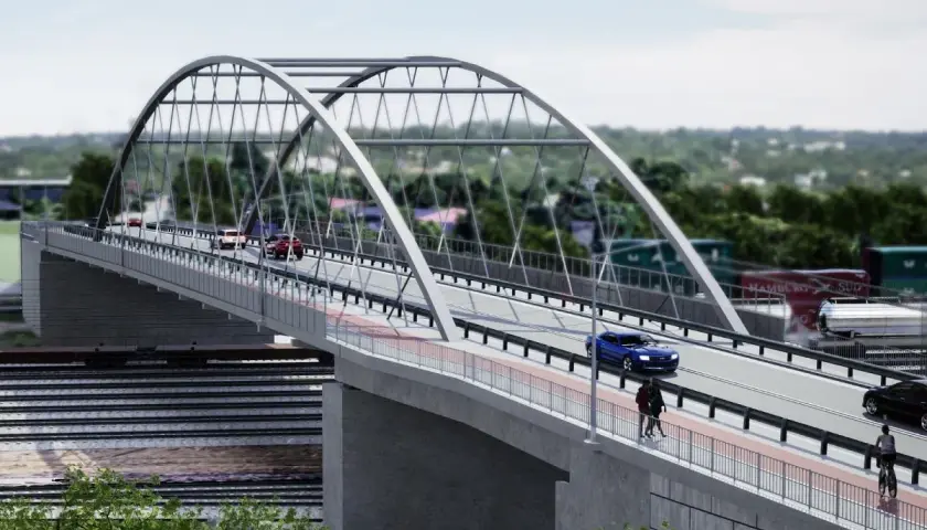 Nowoczesny most nad torami kolejowymi, po którym poruszają się samochody i rowerzyści. W tle widoczne kontenery i zieleń.