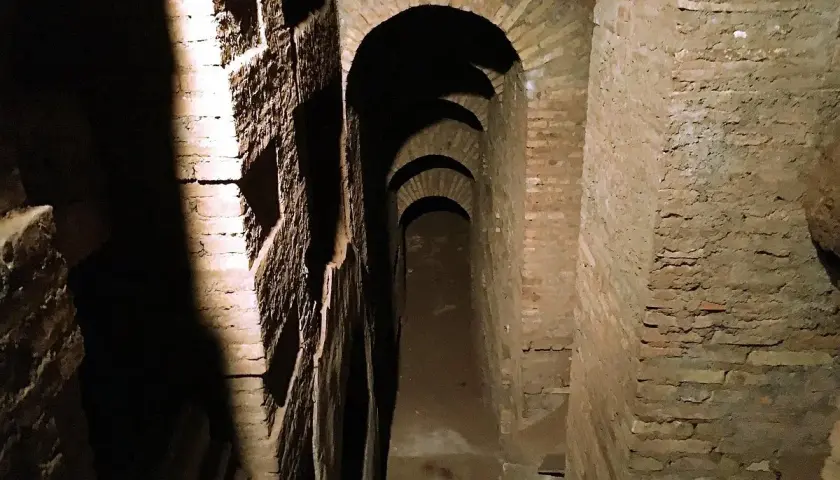 Passage voûté dans les catacombes de Rome, avec des niches creusées dans le mur de briques.