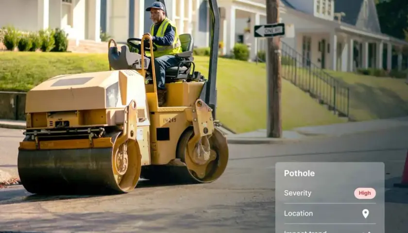 A worker operates a steamroller, ready to be a change agent and fix the high-severity pothole on this street.